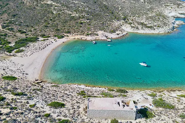 Race2Adventure Greece 2028 global vacation adventure aerial view of a white ship anchored in turquoise waters off the Greek island Polyaigos on a sunny day. Run, seek, adventure!