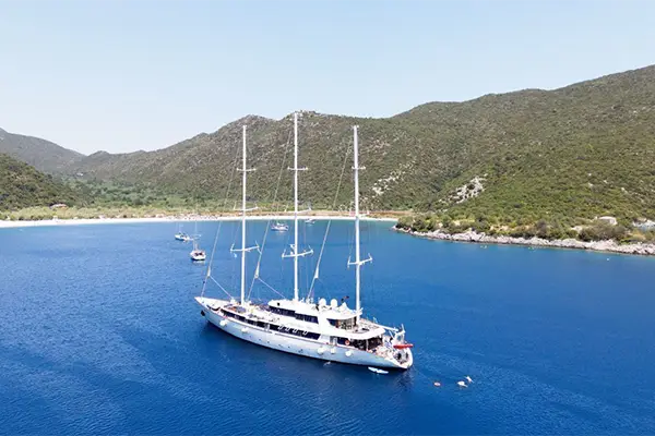 Race2Adventure Greece 2028 global vacation adventure aerial view of a white ship anchored in azure waters off a Greek island on a sunny day. Run, seek, adventure!