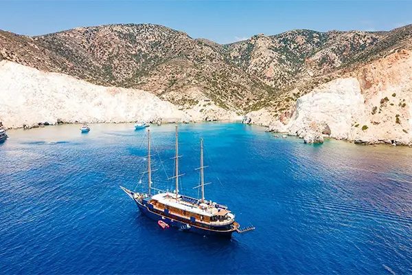 Race2Adventure Greece 2028 global vacation adventure aerial view of a ship anchored in azure waters off a Greek island on a sunny day. Run, seek, adventure!