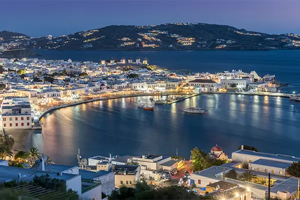 Race2Adventure Greece 2028 global vacation adventure aerial evening view illuminated Greek island Mykonos. Run, seek, adventure!