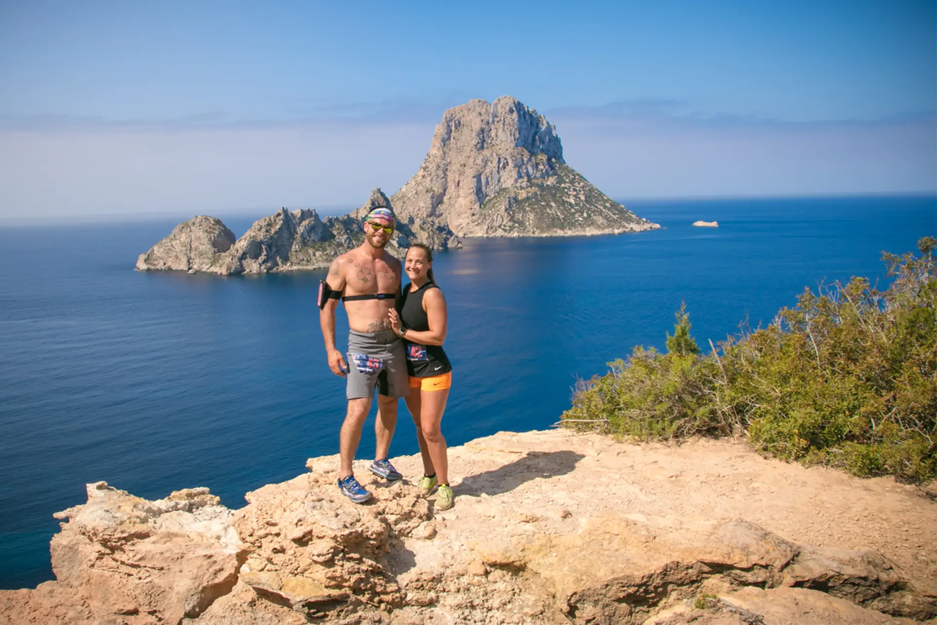 Race2Adventure Greece 2028 global vacation adventure smiling couple on cliff overlooking turquoise waters and cliffs on a sunny day. Run, seek, adventure!